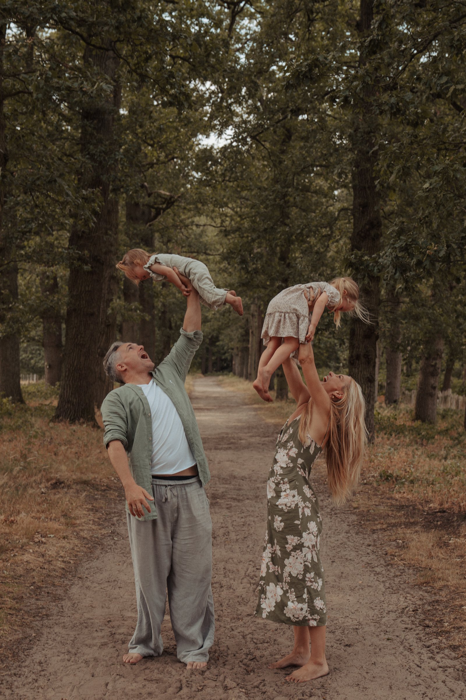 Thomas and Fem Massink lifting their two daughters in the air on a forest path, plant-based family