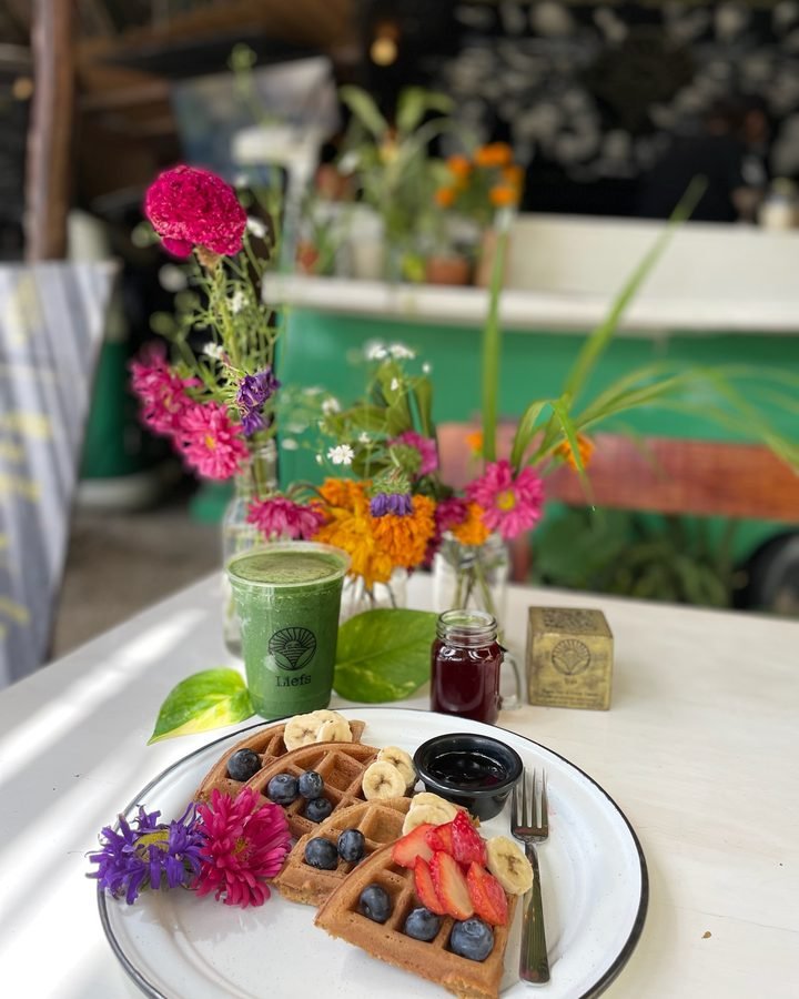 Vegan waffles with banana, strawberries and blueberries beside a green smoothie and edible flowers at Liefs Tulum